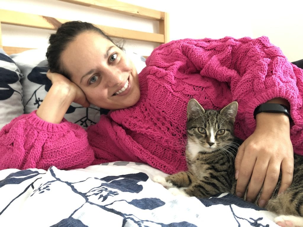 Kate wears a bright pink sweater and lies on her side, holding her little gray tabby kitten, Lewis.