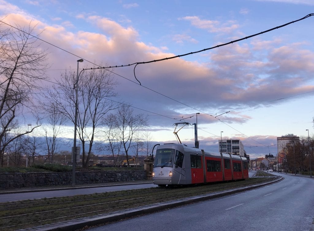 A red and silver tram in Prague running along tracks underneath a blue, pink, and purple sunset sky.