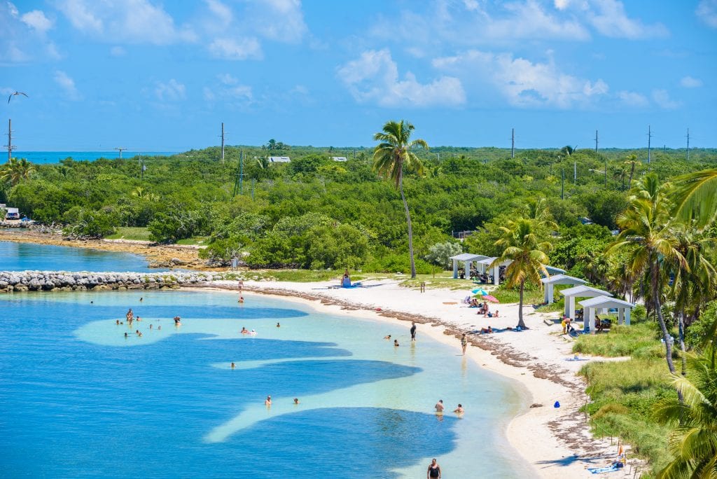 Bright blue clear water leading to the white sandy beach on Bahia Honda State Park.; the land looks like a jungle