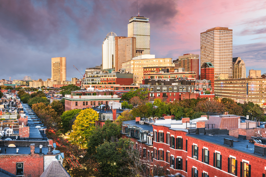 A bright sunset behind the Boston skyline, brownstones in the foreground.