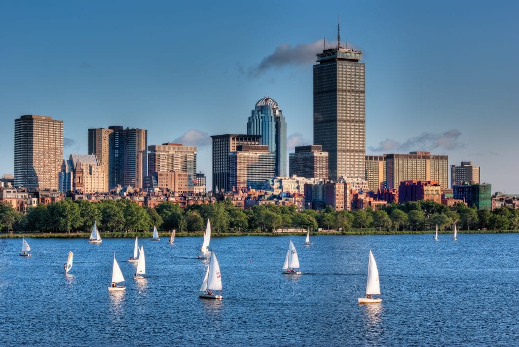 The skyline of Back Bay in the summer, several sailboats sailing along the Charles River.