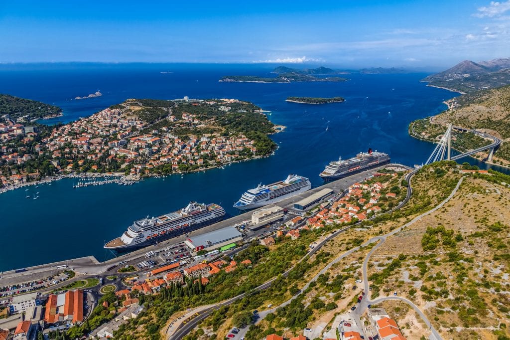 An aerial view of Gruz Harbor in Dubrovnik seen from the top of a mountain. You see three GIANT cruise ships parked in a line. In the background, you see the Kornati Islands poking out of the ocean.