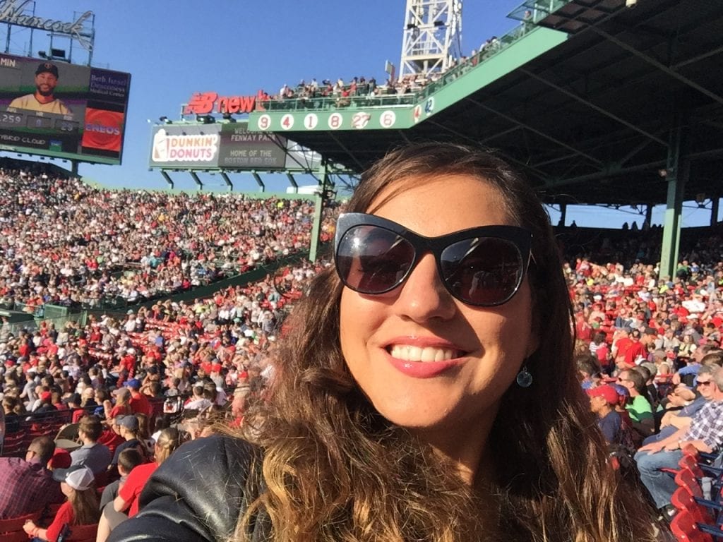 Kate taking a selfie at Fenway park in Boston, thousands of Red Sox fans behind her, many wearing red.