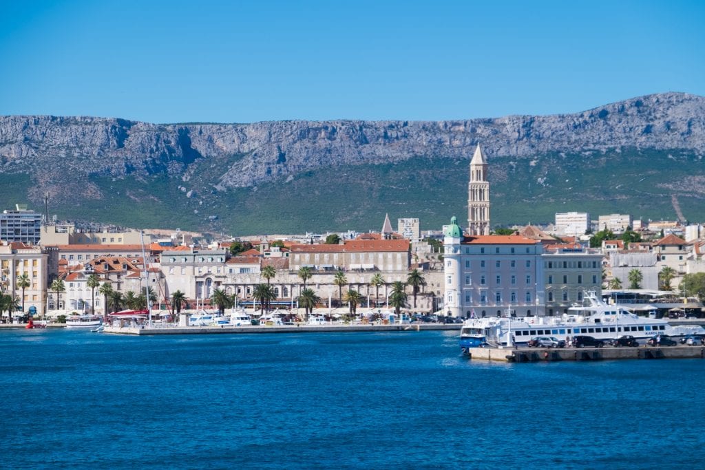 The skyline of Split, all white buildings and orange roofs, against the mountains in the background, the church tower sticking up.