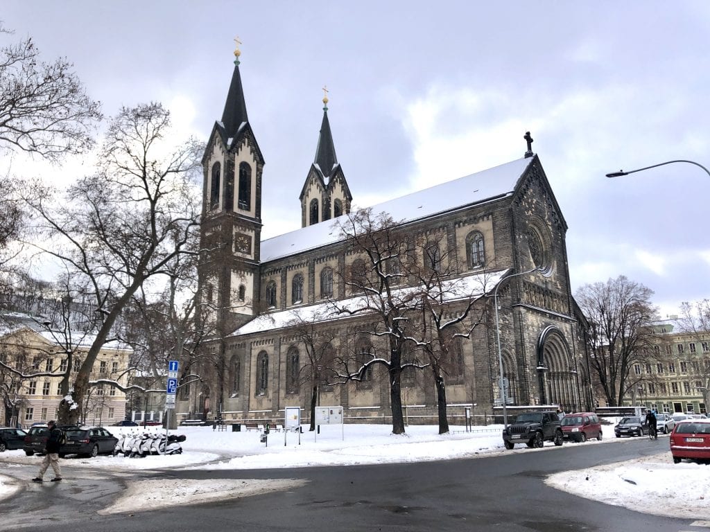 A snow-covered church on a snowy corner in KarlÃn, Prague, underneath a marbled cloudy sky.