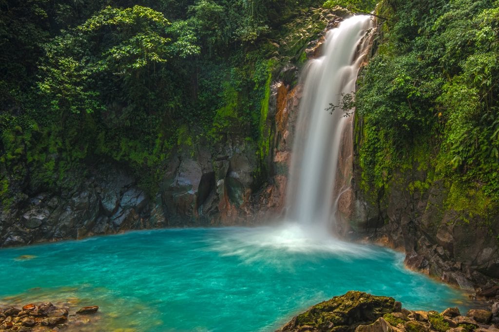 A waterfall in the middle of a jungle, flowing into a bright turquoise pool.