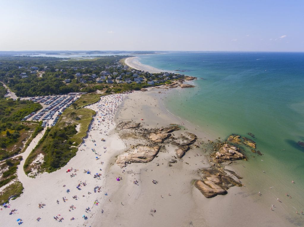 An aerial view of a long sandy beach leading out to calm clear water.