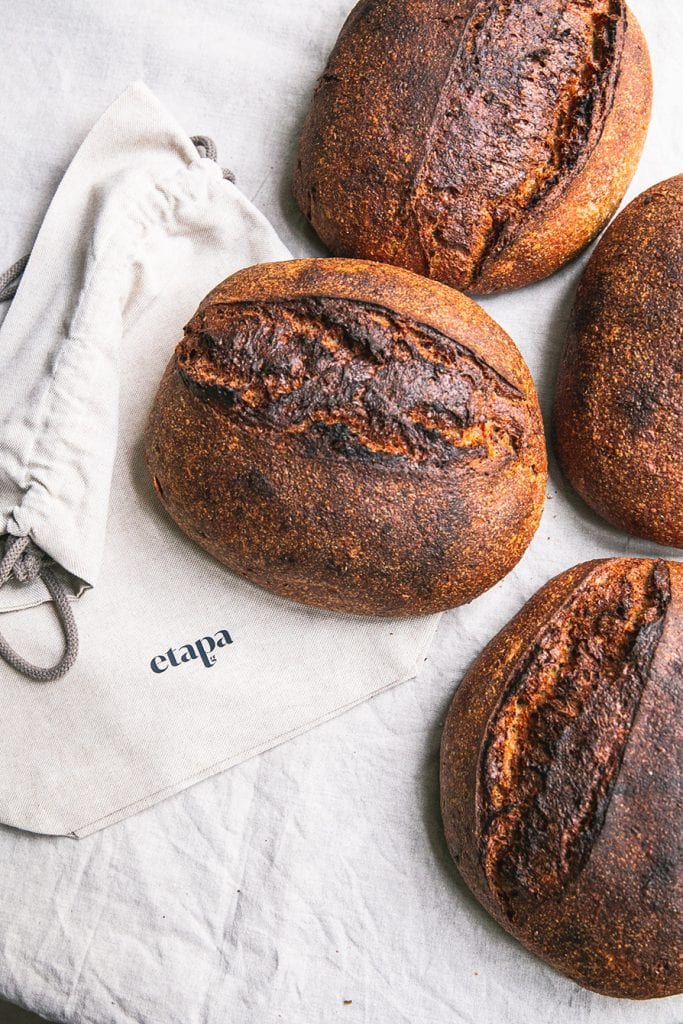 Several loafs of dark brown bread posed next to a napkin that reads "Etapa."