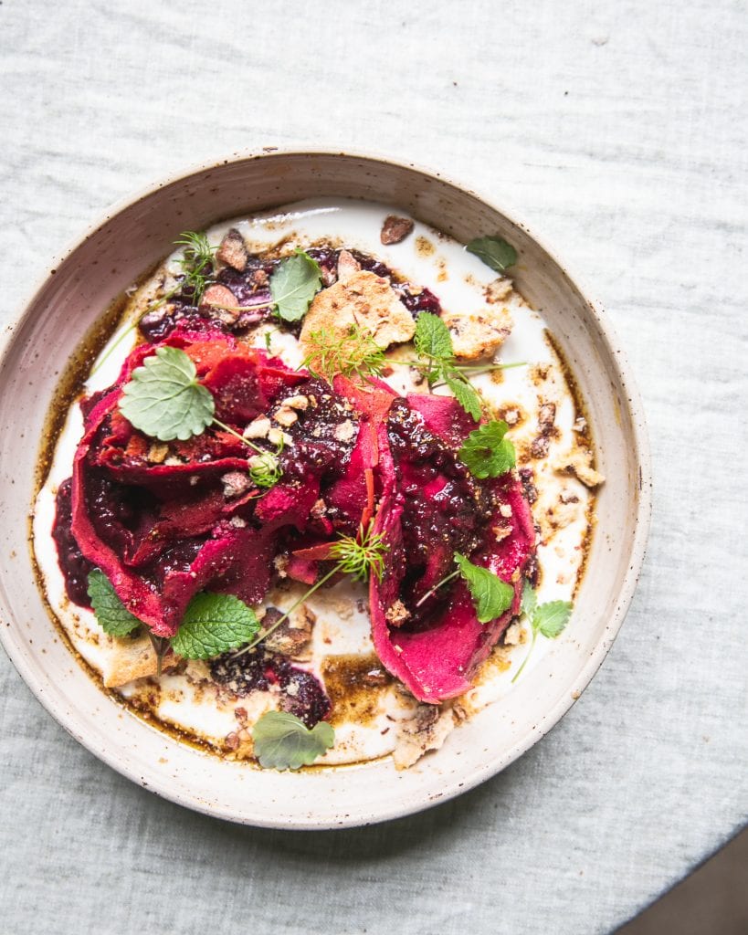 Czech pancakes covered with bright pink paste -- it looks like it's made of beetroot with some pomegranate seeds, nuts, and some parsley as decor.