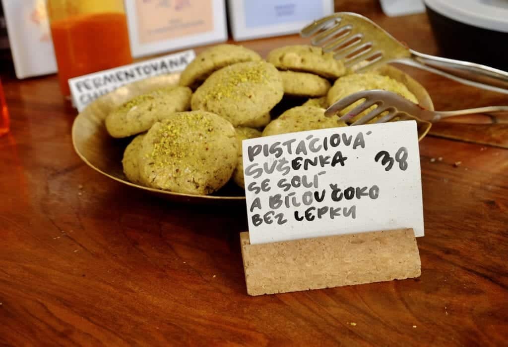 A big plate of cookies topped with pistachio dust, with a card in front describing the dish in Czech. Each cookie costs 38 crowns, about $1.81.