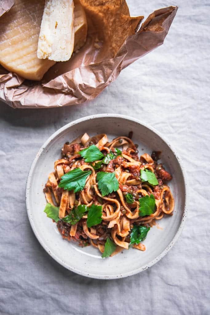 A plate of thick noodles served in what looks like a lentil sauce, topped with parsley leaves.