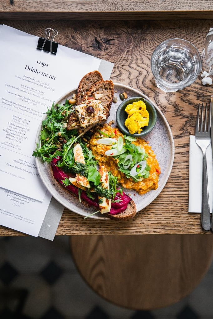 A plate of scrambled eggs topped with green onions, served with thin slices of oblong toast topped with bright pink beet puree, served with salad.