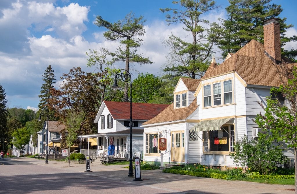 White cottages with signs and awnings on them on a quiet street in Lenox underneath a partly cloudy sky.