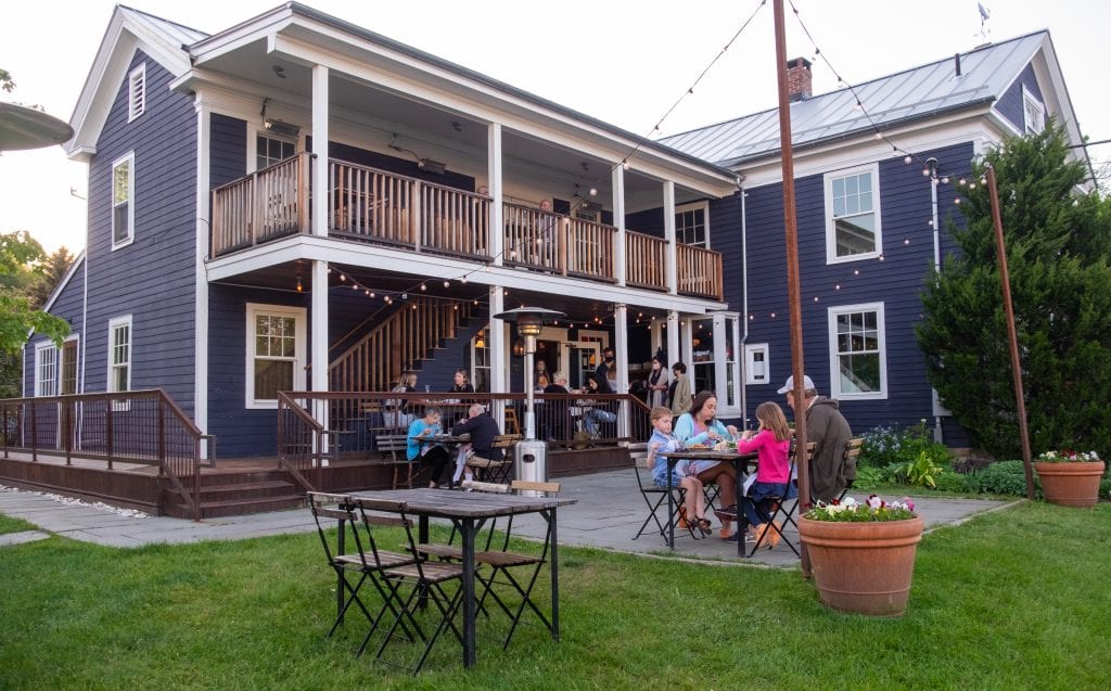 The Prairie Whale restaurant: a big navy blue house and many people eating outside on the porches and on the grass at distanced tables underneath Christmas lights.