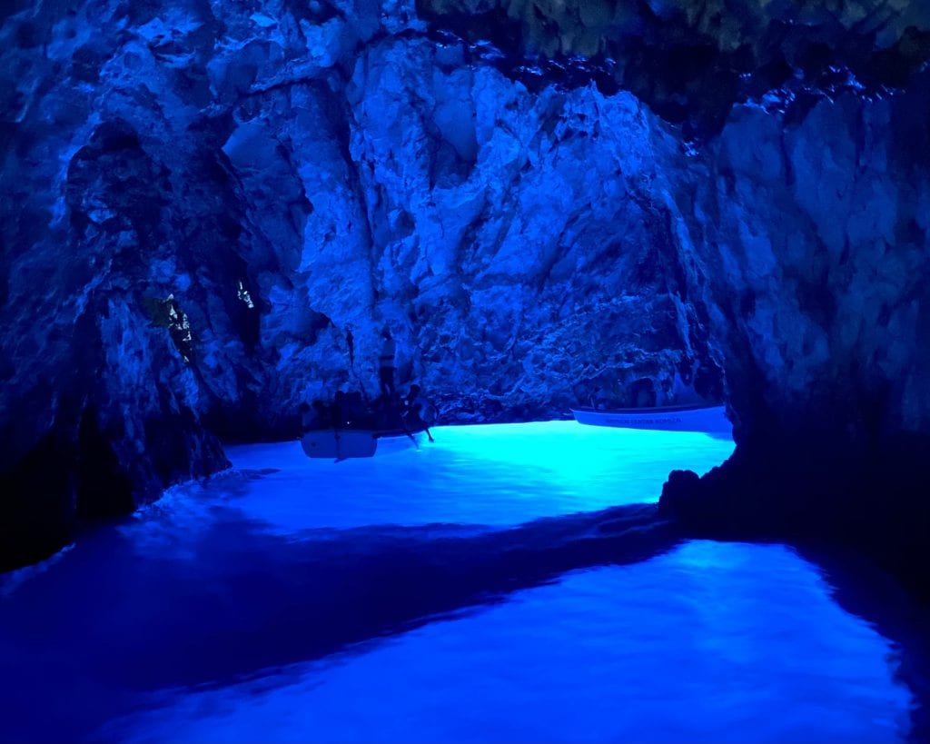 A boat in the back of a water-filled cave glowing bright blue.