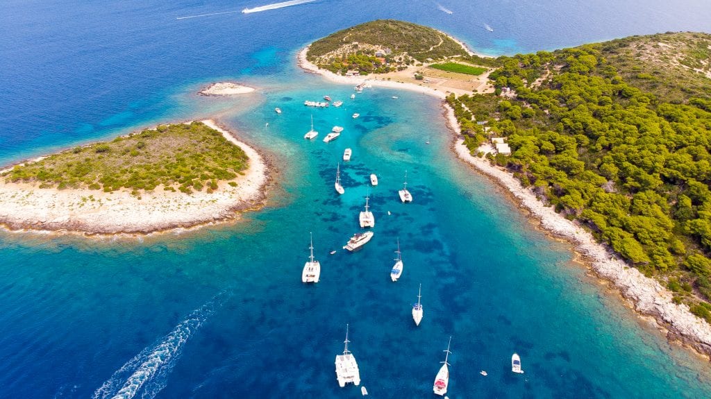 An aerial view of Budikovac, an island surrounded by bright blue water and dotted with several white boats.