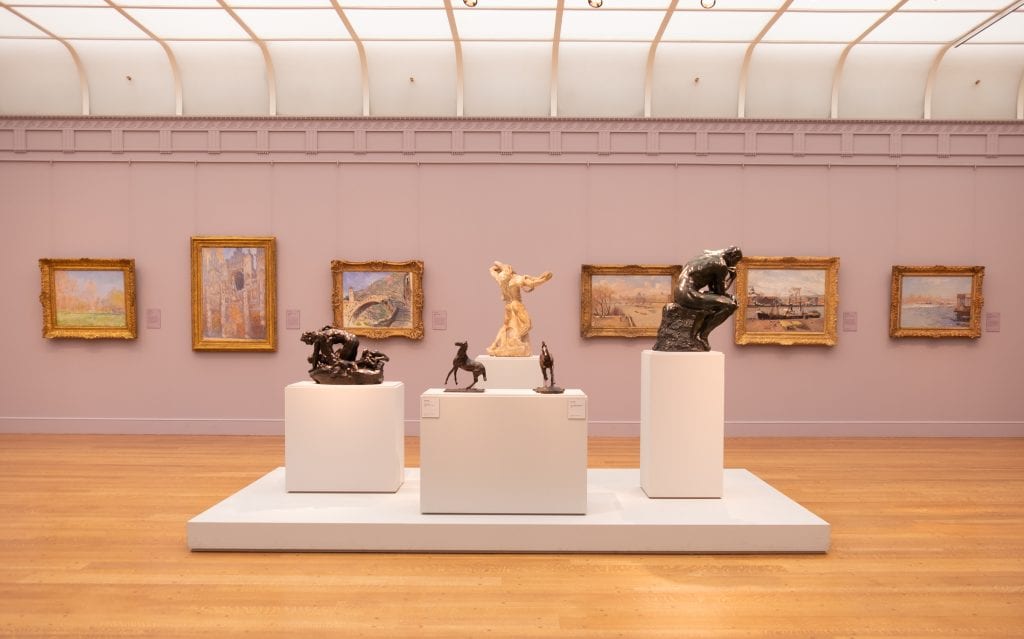 A lavender room with a display of sculptures in front of several Impressionist paintings at the Clark Institute in the Berkshires.