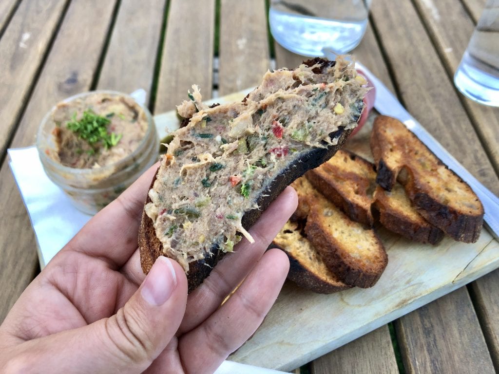 Kate's hand holding a piece of crostini smeared with pork rillette (pork terrine mixed with several vegetables).