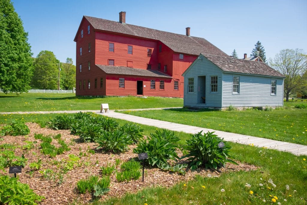 Two 19th century wooden homes, one blood red and one robin's egg blue, perched on a grassy landscape.