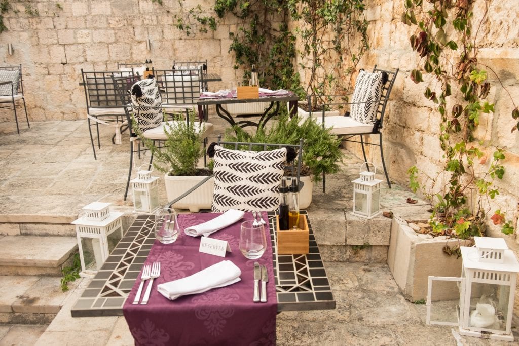 Another angle of the courtyard, tables covered with purple placemats, and plants and large white candle-filled lanterns on the ground.