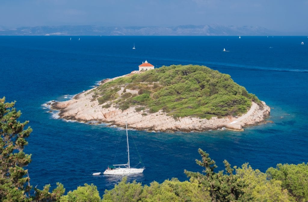 A teeny tiny island with a single orange-roofed building on it. In the foreground, a sailboat.