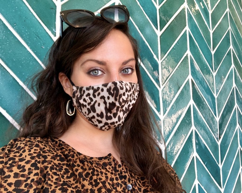 Kate standing in front of a teal tiled wall, wearing a leopard print shirt and leopard print face mask.