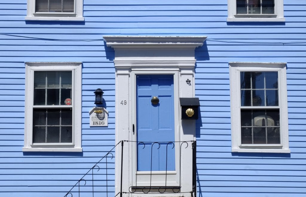 A periwinkle-blue house in Marblehead, Massachusetts, with a small plaque bearing 1810 John Goodman and a bright gold fish. On the mailbox is a bright gold seashell.