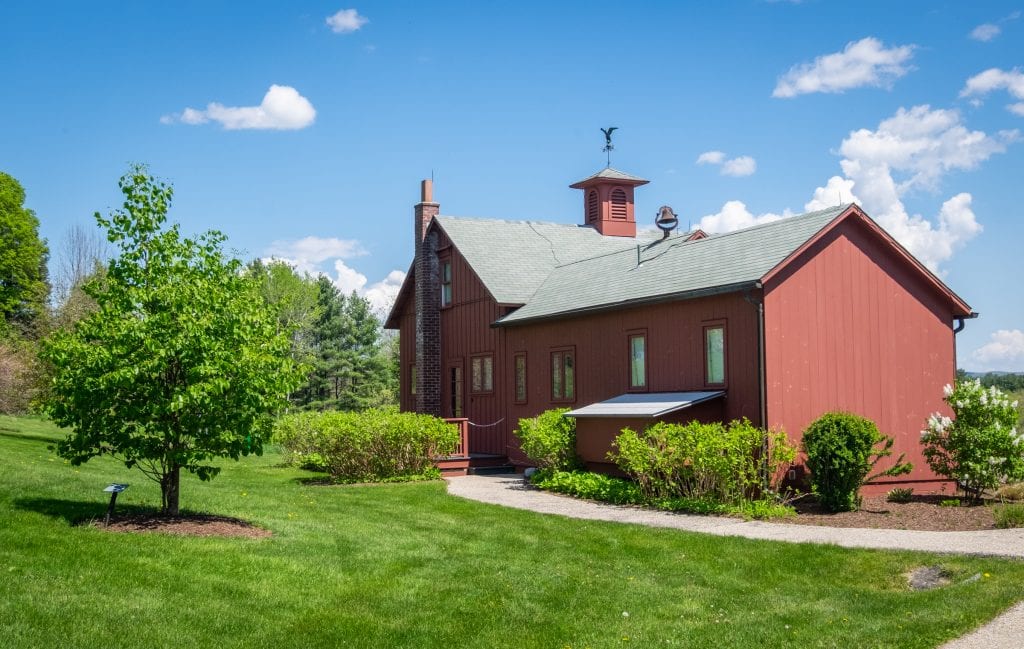 Norman Rockwell's little red cabin, sitting in a grassy area underneath a blue sky with a few clouds.