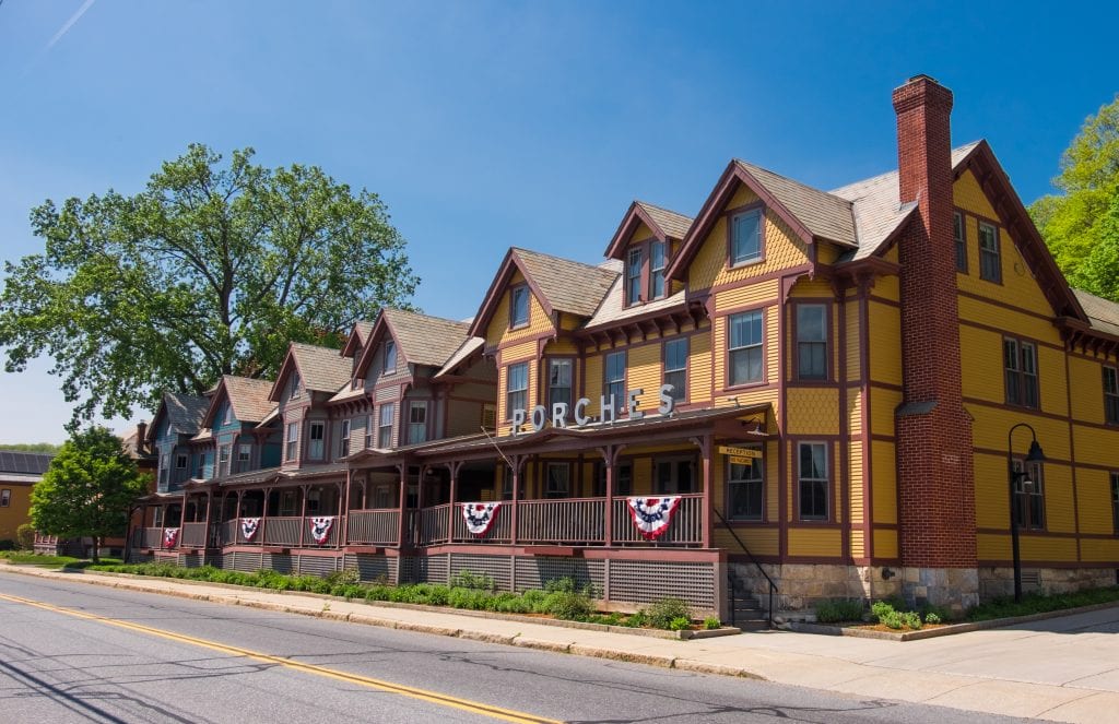 Porches: four Victorian homes joined together with a big wooden porch in front. One is blue, one is gray, and one is yellow, all with brown trim.