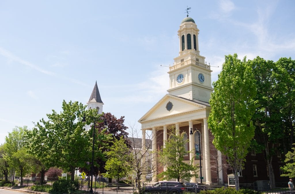 A brick building with tall ivory-colored columns and a clock tower in downtown Pittsfield.