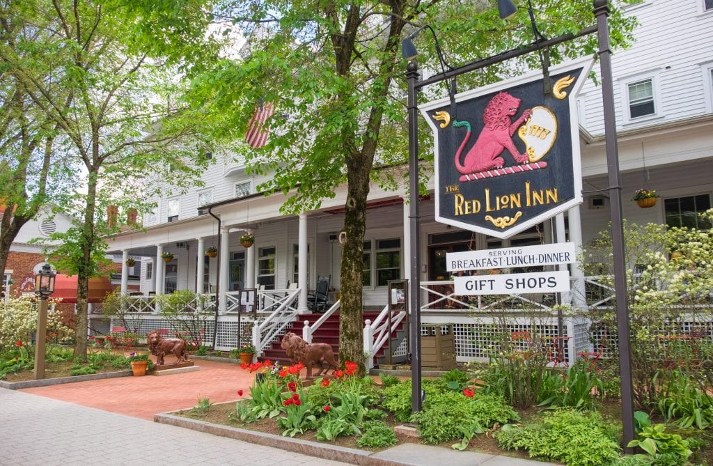 An old-fashioned in with a big porch, and a sign reading Red Lion Inn with a red lion on it.