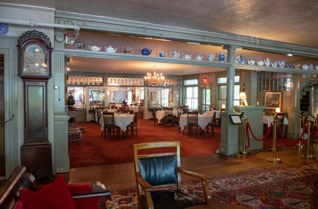 The entrance to the dining room at the Red Lion -- you see tables covered with white tableclothes, old-fashioned chandeliers, a dark wooden grandfather clock, and a shelf lined with all kinds of old-fashioned teapots for decoration.