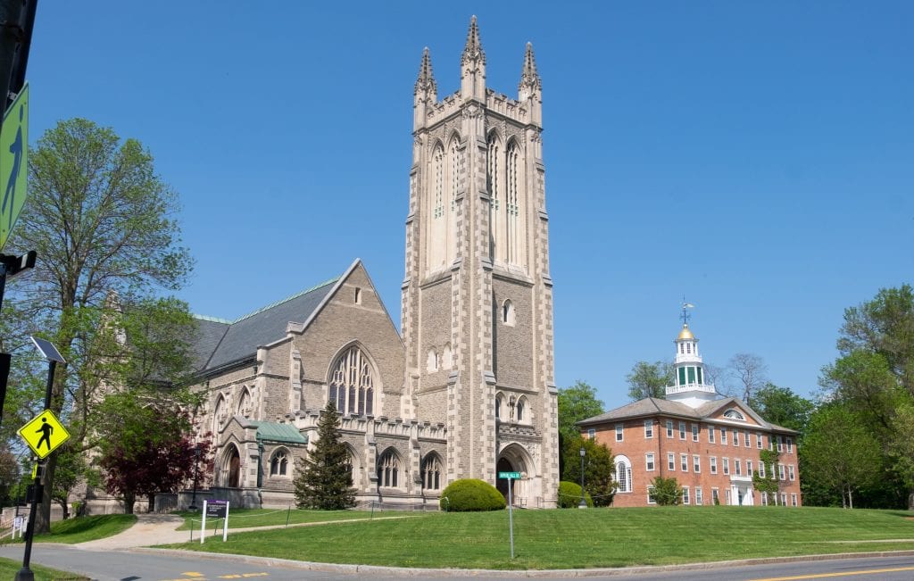 Two buildings in the tiny town of Williamstown: a big gray church with a tall bell tower, and a smaller red brick building with a tiny gold dome and weathervane.