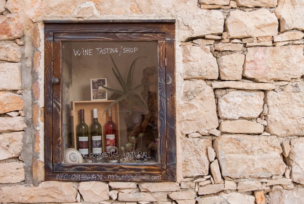 A rock wall in Vis town, with a window that has wine bottles inside and reads "Wine Tasting/Shop."