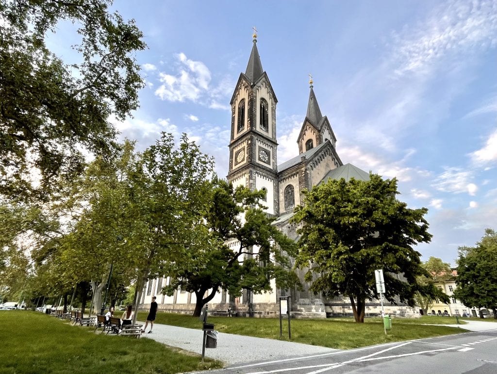 A two-towered church on my home square in Karlin, Prague, surrounded by trees and grassy spaces.