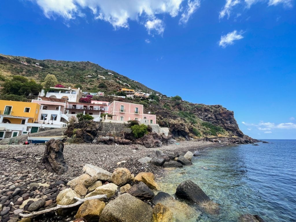 A gray pebbly beach with a few small pastel-colored buildings on Alicudi.