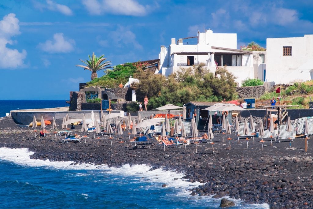 beach chairs perched on a black rocky beach in Stromboli, Italy.