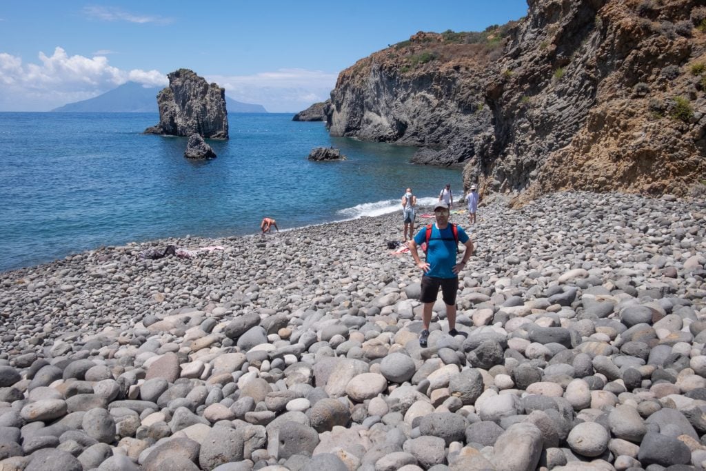 Charlie standing on giant gray rocks, nearly boulders, each about 12 inches wide, in Cala Junco, Panarea.