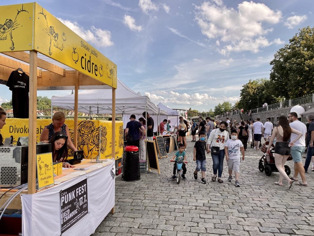 A crowd of people along the riverside in Prague, buying cider at cider stands for Cider Fest.