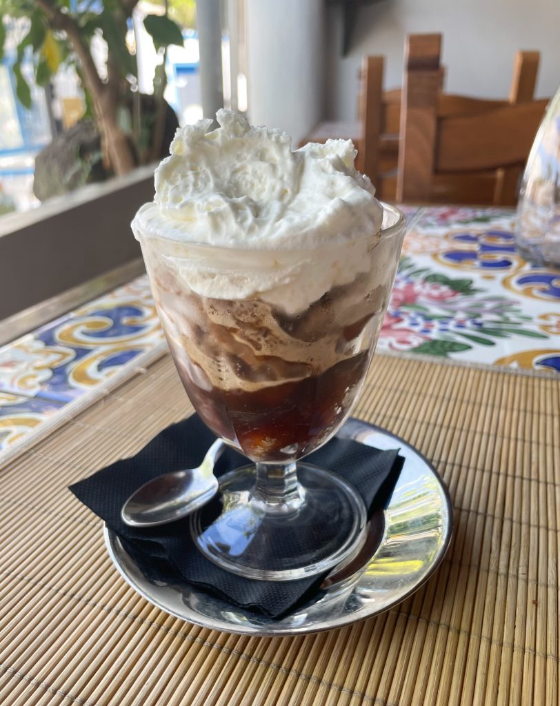 A clear bowl of coffee granita topped with extra thick whipped cream.