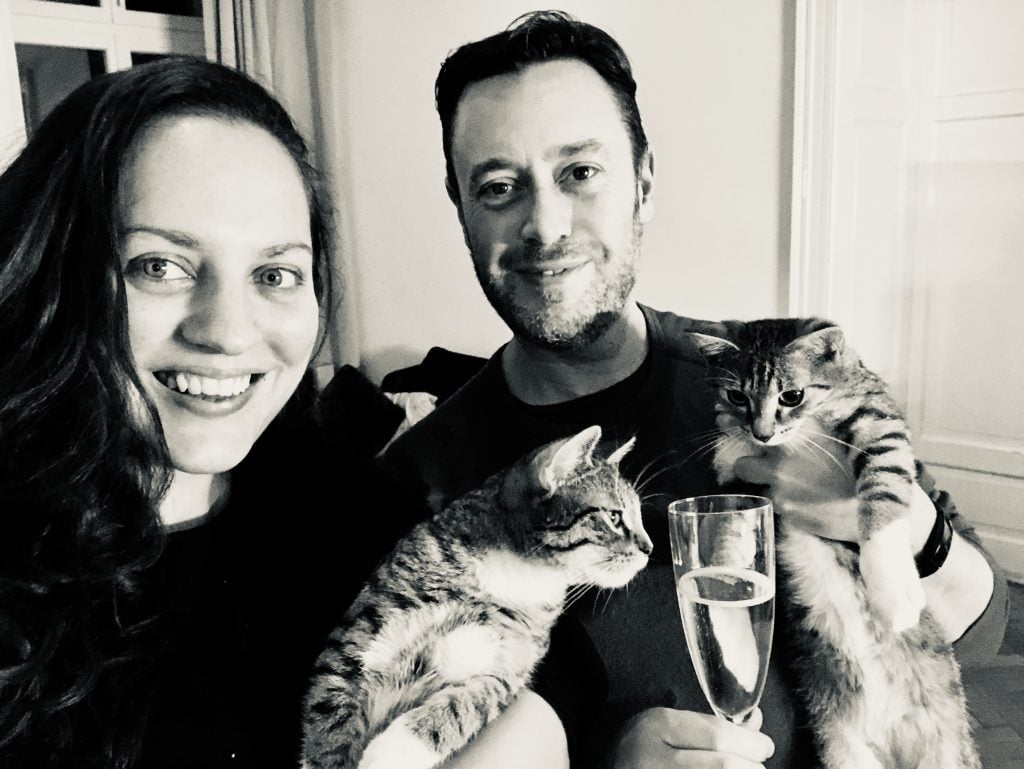 Kate and Charlie taking a selfie, holding champagne, each one holding a kitten. The kittens are very interested in the champagne.
