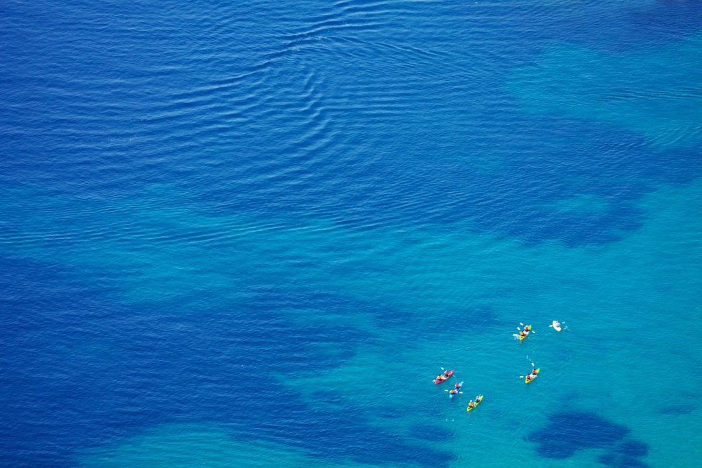 An aerial shot of several kayakers in the bright blue sea.