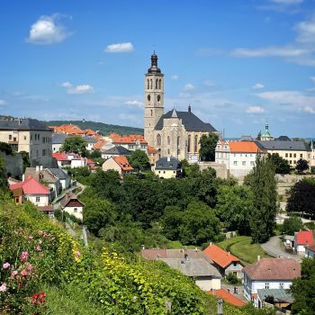 The bohemian city of Kutna Hora, with a church tower, green hills, and lots of orange-roofed buildings.