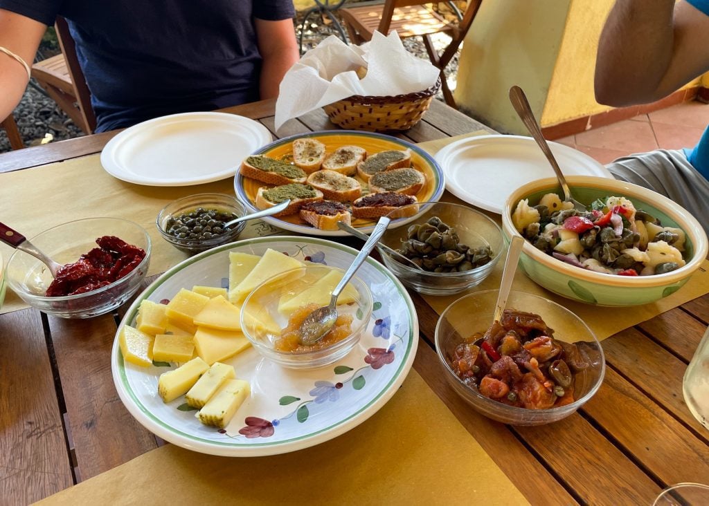 Plates and platters of capers, sun-dried tomatoes, several cheeses with honey, crostini with all kinds of spreads, and Aeolian potato salad with capers and tomatoes.