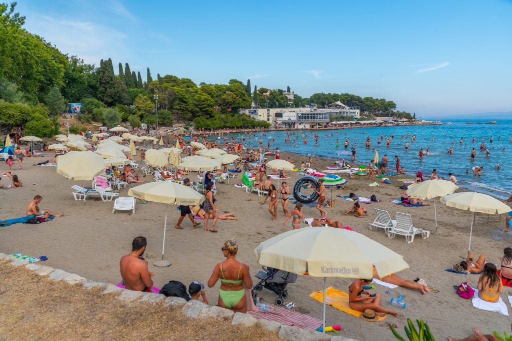 Hundreds of people clustered on a sandy beach in Split. One girl looks like her butt is eating her bathing suit. Oh dear.