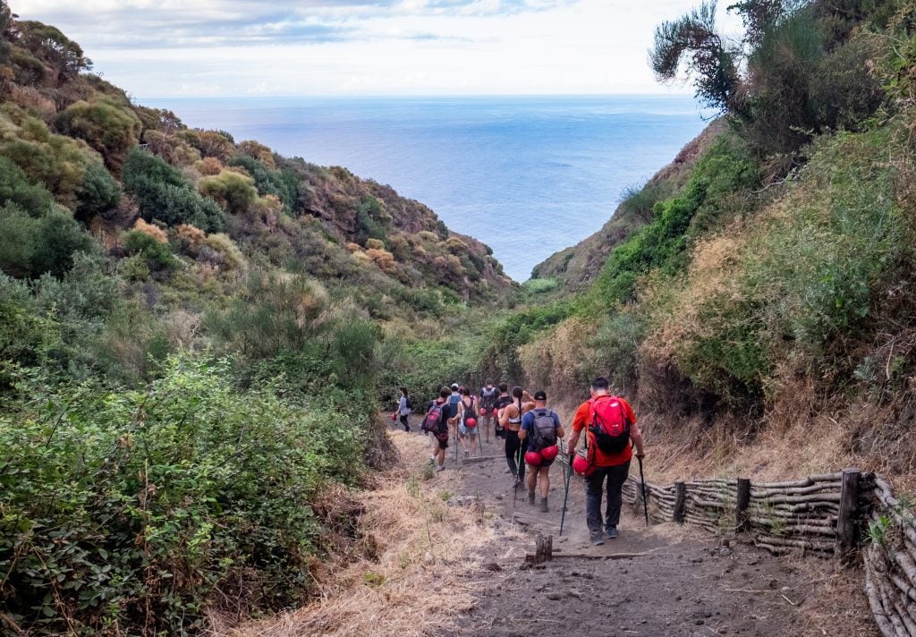 A group of hikers heading downhill with hiking poles, unused helmets dangling off their backpacks.