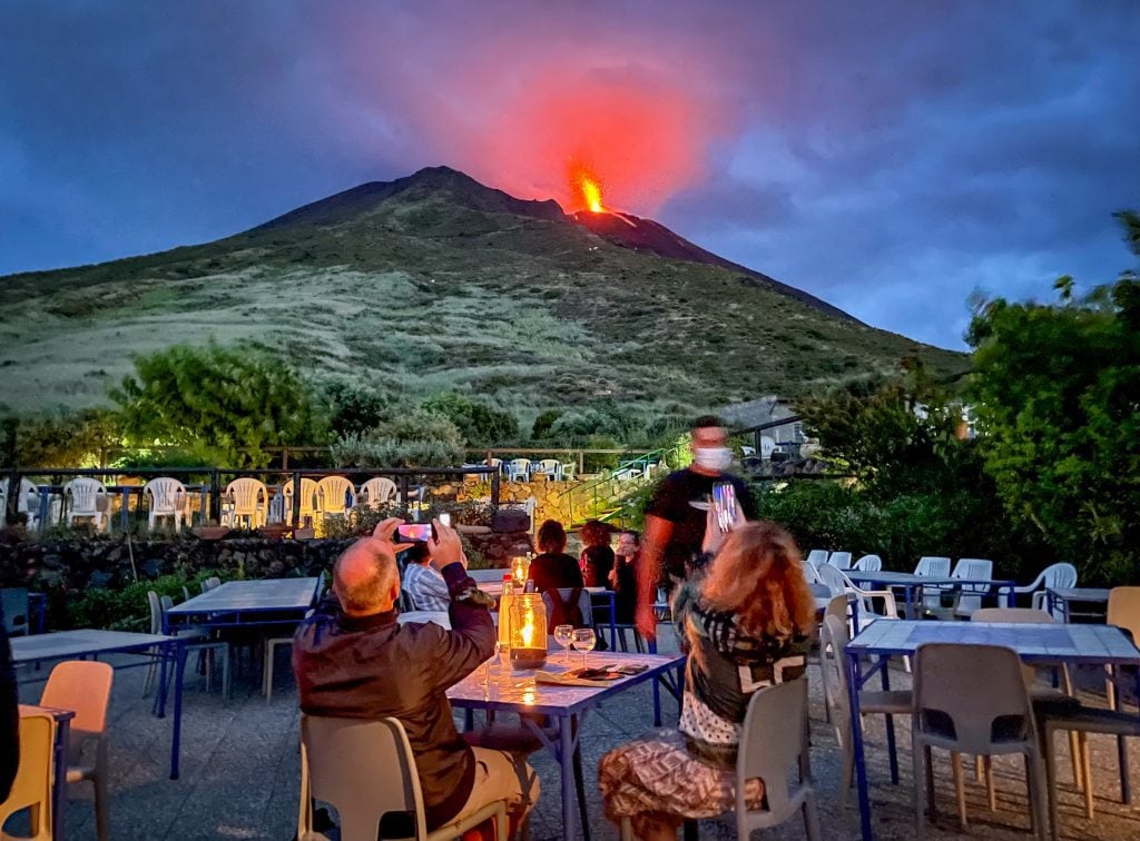 Having dinner outside at Osservatorio restaurant, watching a volcano erupt with plumes of lava in the background.