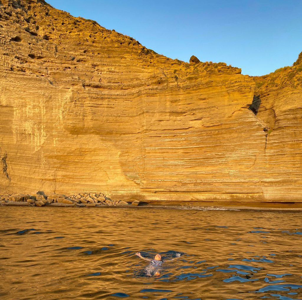 Kate swimming in the ocean, the bright orange lined cliffs of Pollara rising in the warm sunset light.