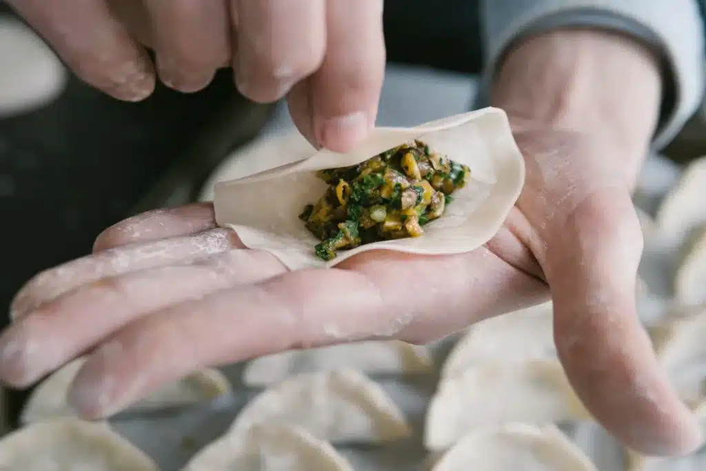 A hand folding a dumpling wrapper around a filling of meat and vegetables.
