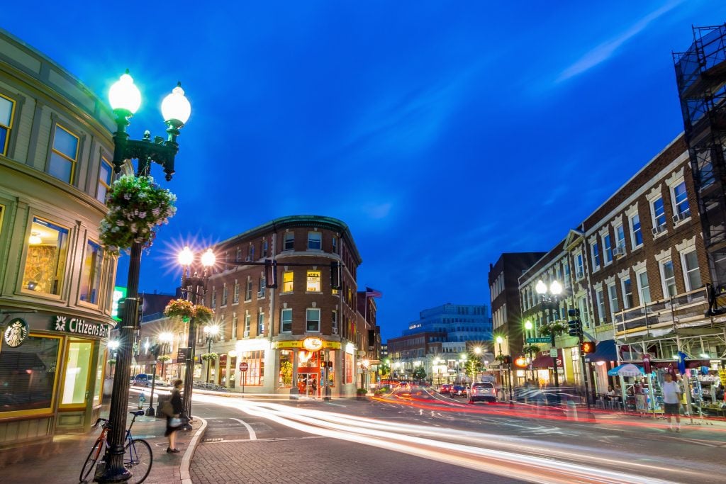 Harvard Square at night underneath a dark blue sky, people walking around.